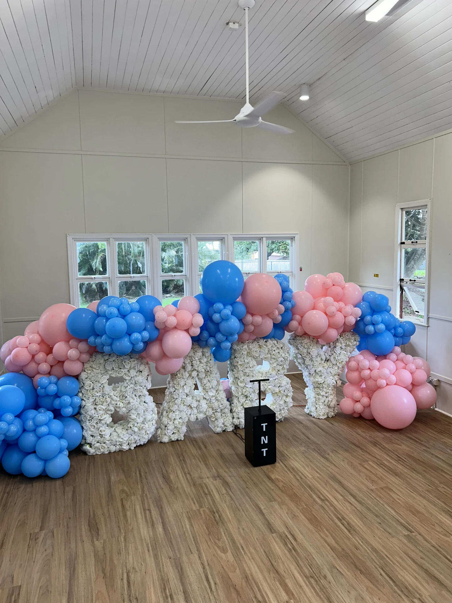 Indoor gender reveal display with pink and blue balloons, OH BABY letters and a TNT box