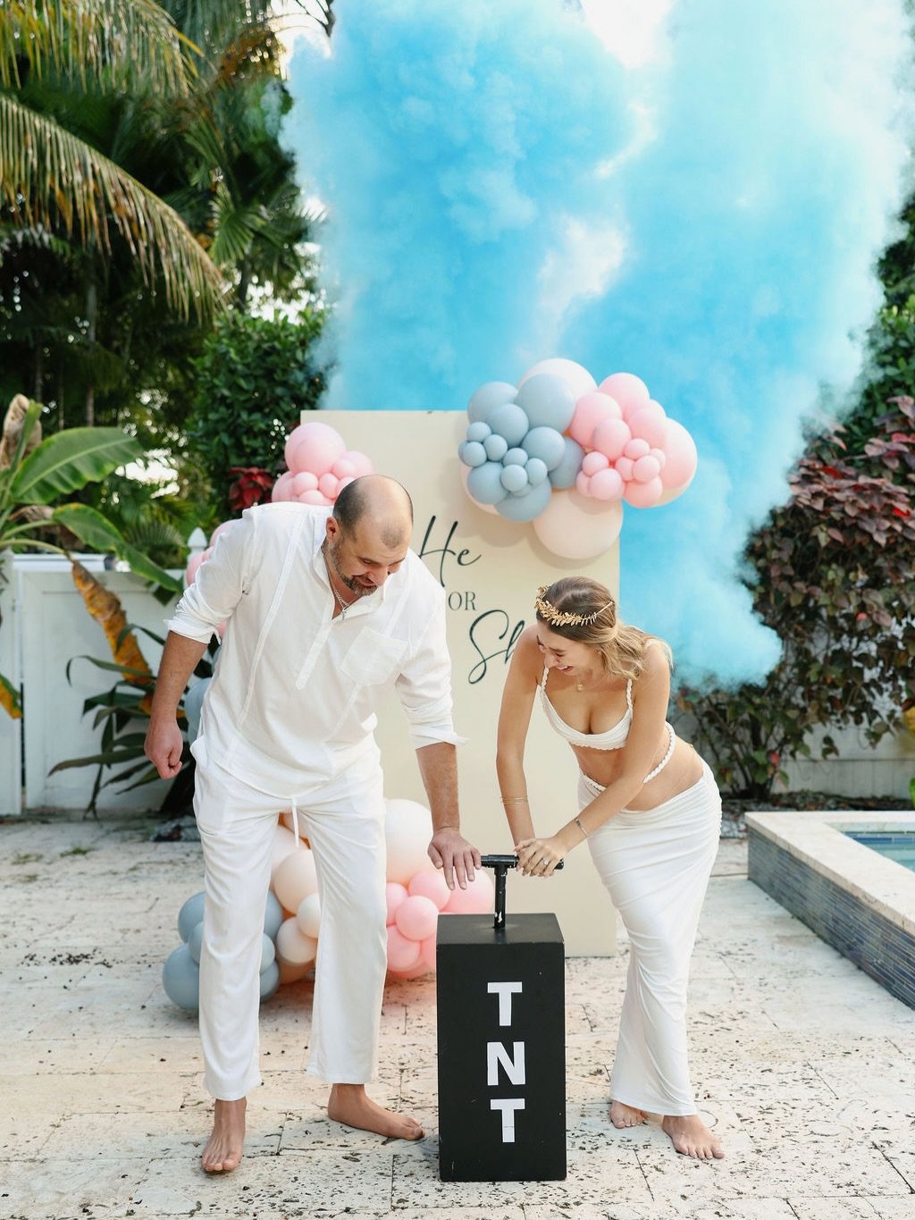 Couple at a TNT gender reveal with a blue powder cloud and balloon display