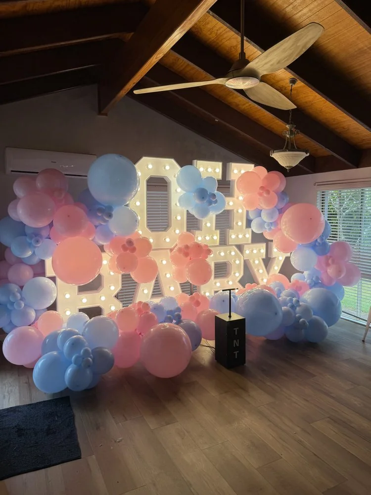 Indoor gender reveal display with pink and blue balloons, OH BABY letters and a TNT box