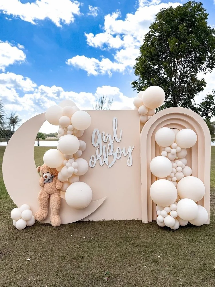 Outdoor gender reveal backdrop with pale balloons, a crescent moon and a teddy bear