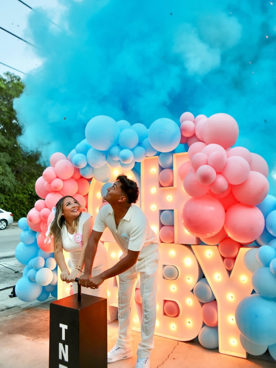 Couple at a TNT gender reveal with blue powder, balloons and illuminated BABY letters