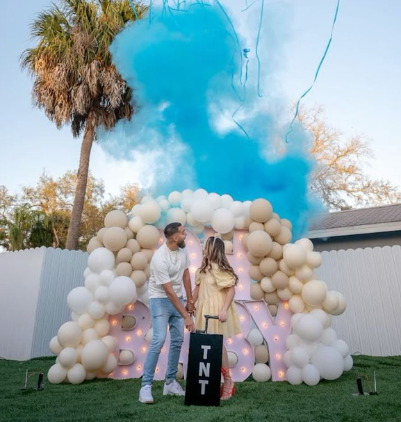 Outdoor gender reveal with blue powder, pale balloons and a TNT box